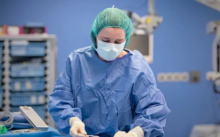 Nhân viên y tế mặc áo choàng vô khuẩn và đeo găng tay phẫu thuật trong phòng mổ