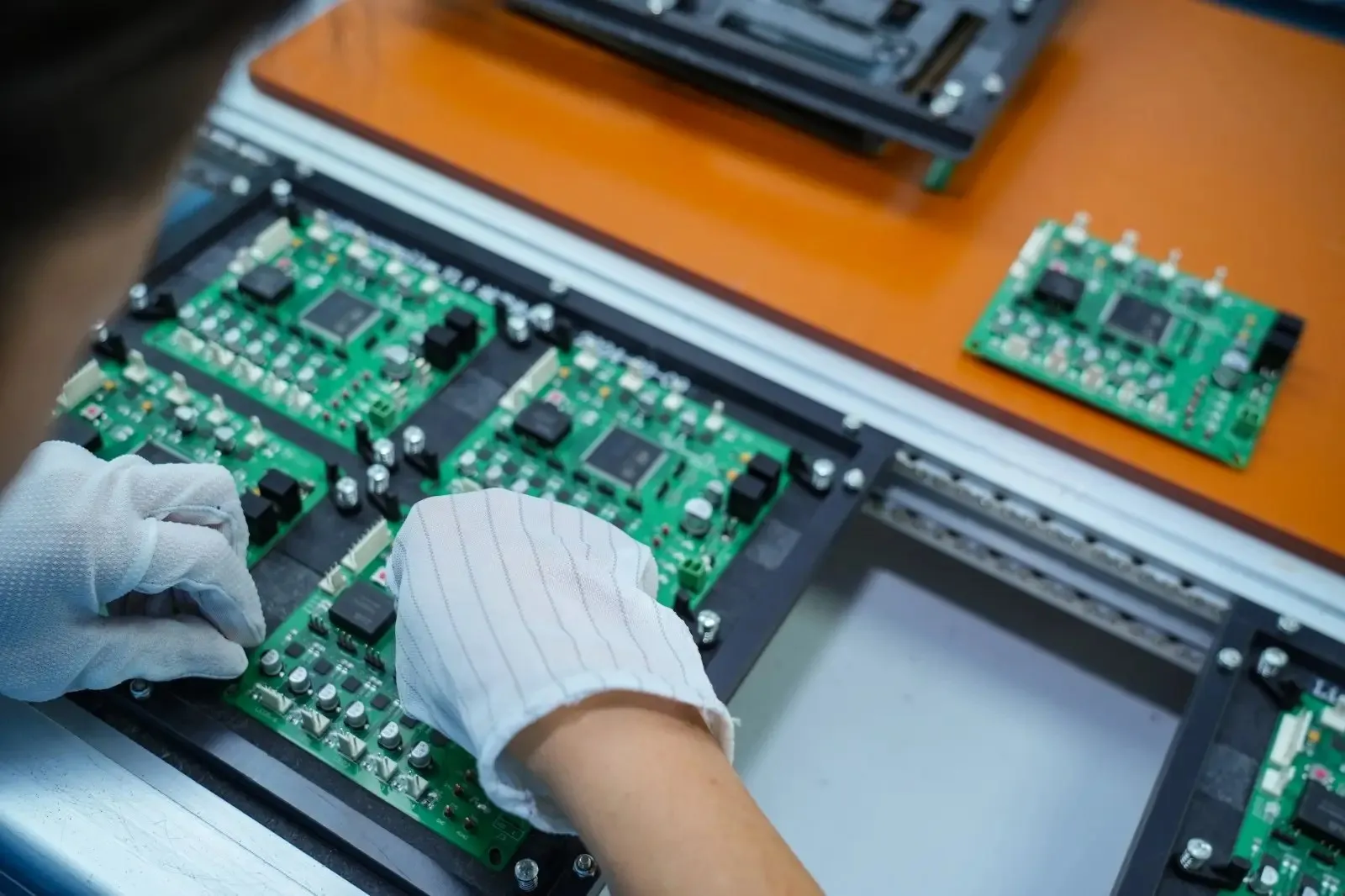 Công nhân đeo găng tay chống tĩnh điện sọc sợi carbon đang cầm và lắp bo mạch PCB trong nhà máy điện tử