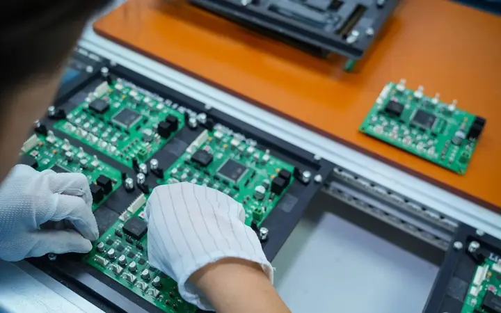 Công nhân đeo găng tay chống tĩnh điện sọc sợi carbon đang cầm và lắp bo mạch PCB trong nhà máy điện tử