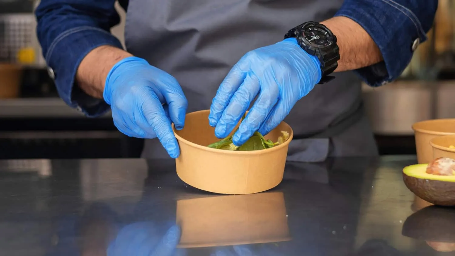 Nhân viên bếp đeo găng tay nitrile xanh trộn salad trong hộp giấy