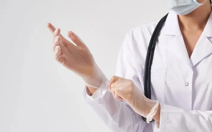 Bác sĩ mặc áo blouse trắng đang đeo găng tay y tế trong suốt trước khi khám bệnh