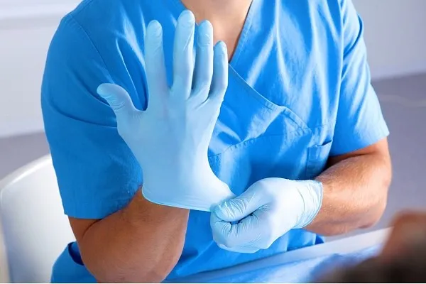 Nhân viên y tế đang đeo găng tay cao su xanh nhạt vào tay