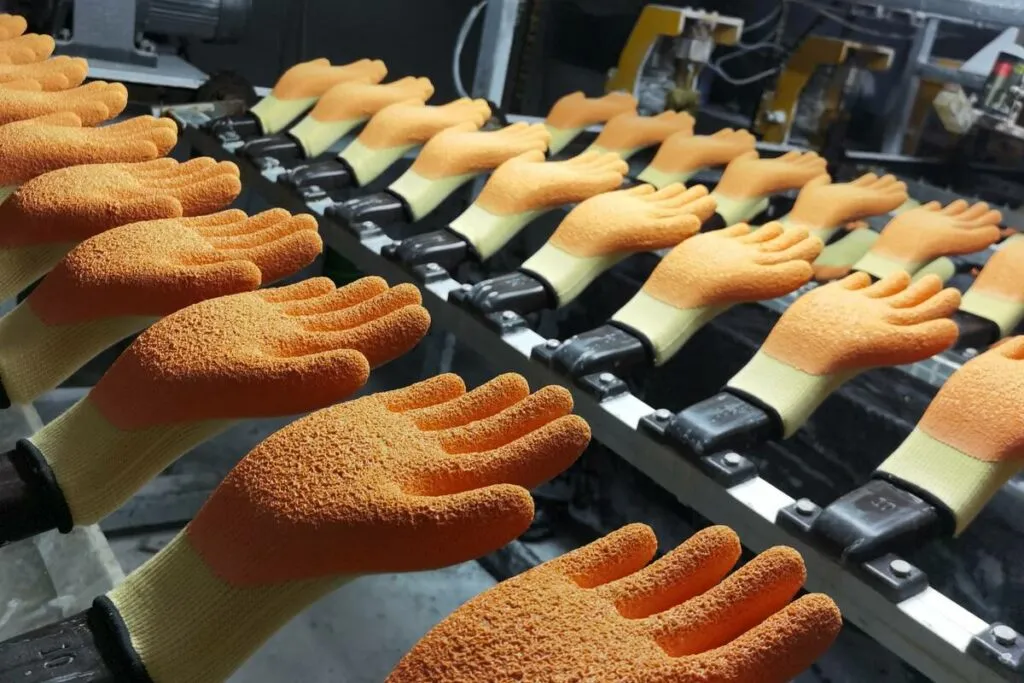 Hàng găng tay bảo hộ dệt kim phủ latex màu cam đang di chuyển trên dây chuyền phủ trong xưởng sản xuất